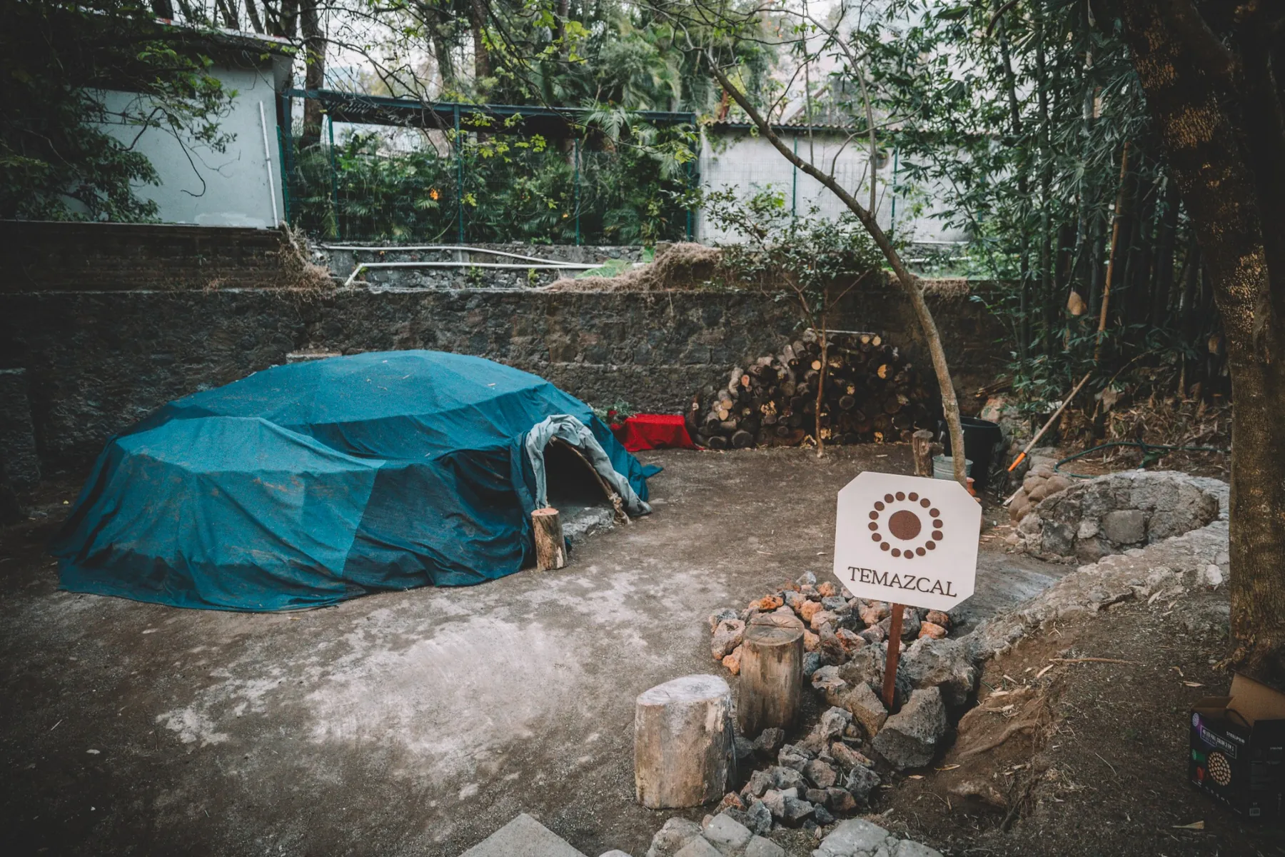 Domo del temazcal con leña y señalética en el jardín de IKAL